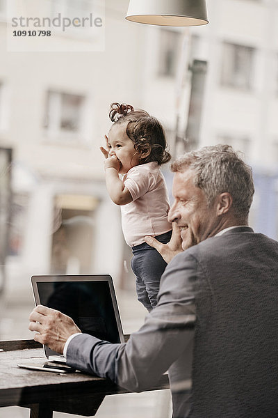 Geschäftsmann mit kleiner Tochter bei der Arbeit am Laptop im Cafe