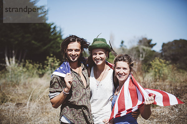 Porträt von drei lächelnden Hippies mit US-Flagge in der Natur