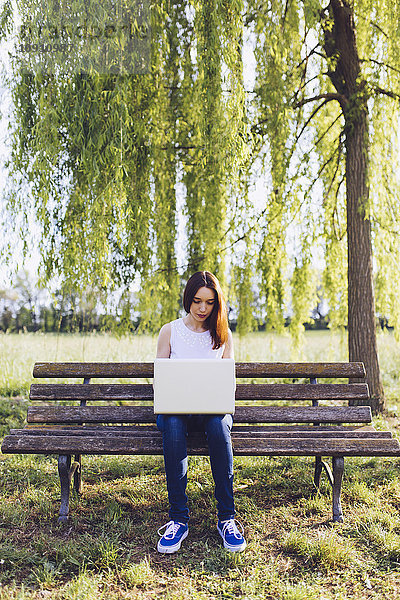 Frau lernt am Laptop  während sie auf einer Bank im Park sitzt.
