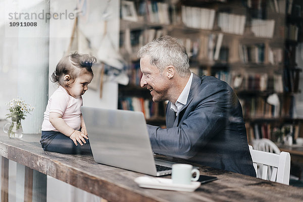 Geschäftsmann mit kleiner Tochter bei der Arbeit am Laptop im Cafe