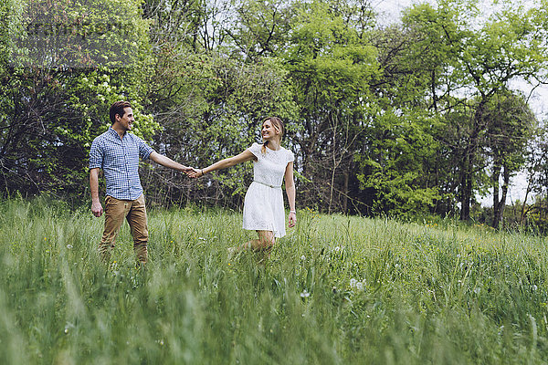 Verliebtes Paar hält sich beim Spaziergang auf einer Wiese an den Händen.