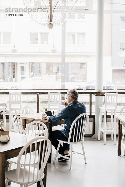 Erwachsener Mann mit digitaler Tablette und Kaffee im Café