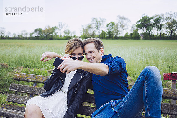 Paar  das auf einer Bank sitzt und Selfie mit Smartphone nimmt