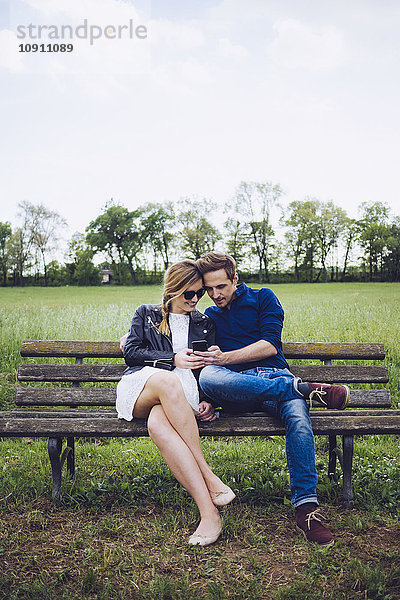 Paar sitzt auf einer Bank und schaut auf das Smartphone.