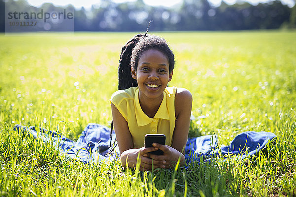 Porträt einer jungen Frau mit Smartphone  die sich auf einer Wiese ausruht