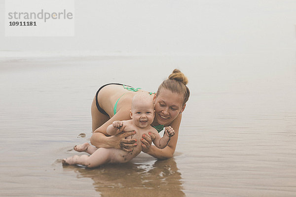 Mutter und Kind spielen im Wasser am Strand