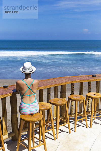 Indonesien  Bali  Junge Frau auf Barhocker am Strand sitzend