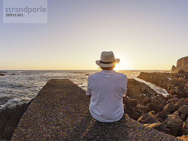 Portugal  Älterer Mann am Hafen bei Sonnenuntergang an der Wand sitzend