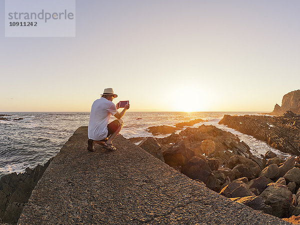 Portugal  Senior an der Wand im Hafen bei Sonnenuntergang  Fotografieren mit digitalem Tablett