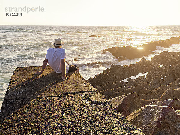 Portugal  Älterer Mann am Hafen bei Sonnenuntergang an der Wand sitzend