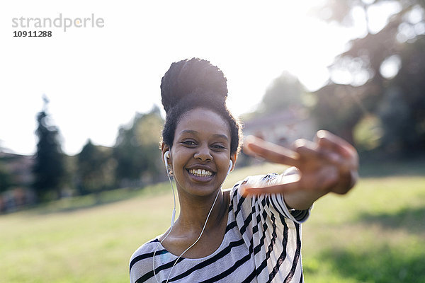 Porträt einer fröhlichen Frau  die Musik mit Kopfhörern mit Siegeszeichen hört
