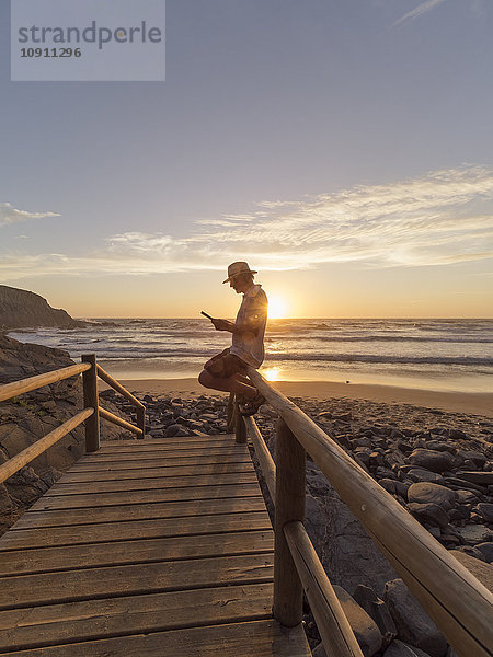 Portugal  älterer Mann auf einem Geländer am Strand sitzend  lesend