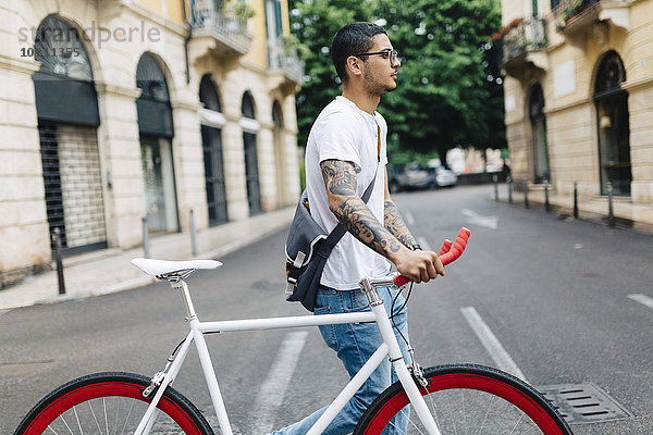 Junger Mann zu Fuß mit dem Fahrrad in der Stadt