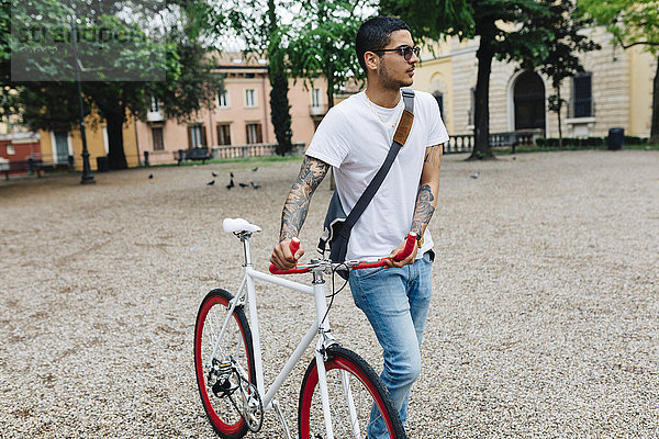 Junger Mann zu Fuß mit dem Fahrrad in der Stadt