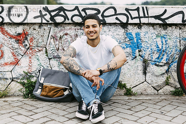 Lächelnder junger Mann an der Graffiti-Wand sitzend