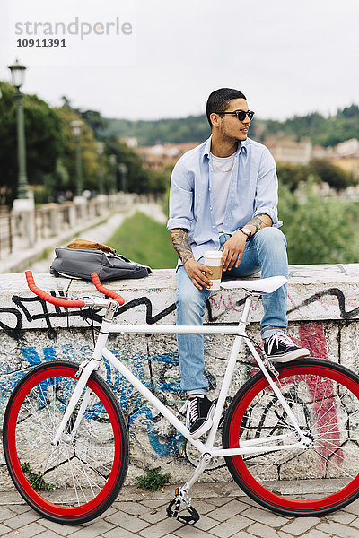 Junger Mann mit Fahrrad auf Graffiti-Wand sitzend