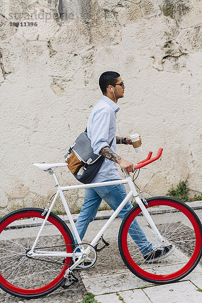 Junger Mann zu Fuß mit dem Fahrrad in der Stadt