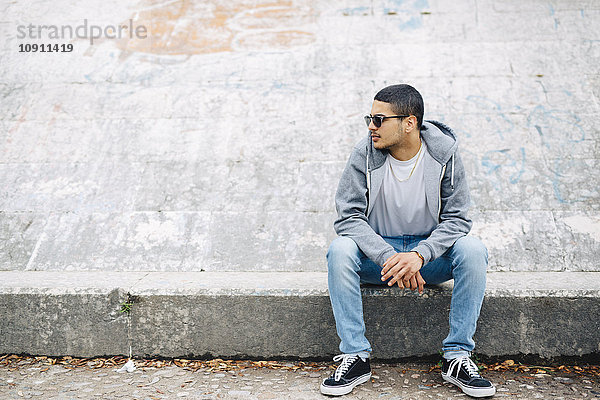 Junger Mann auf einer Wand sitzend mit Kapuze