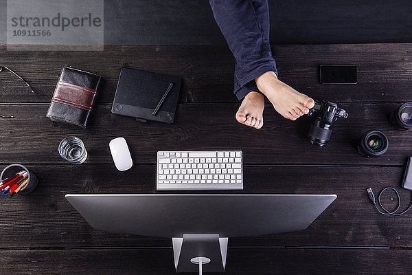 Mann am Schreibtisch sitzend mit Computer und Kamera mit erhobenen Füßen