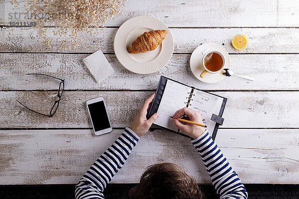 Mann arbeitet mit Smartphone und persönlichem Organizer während des Frühstücks