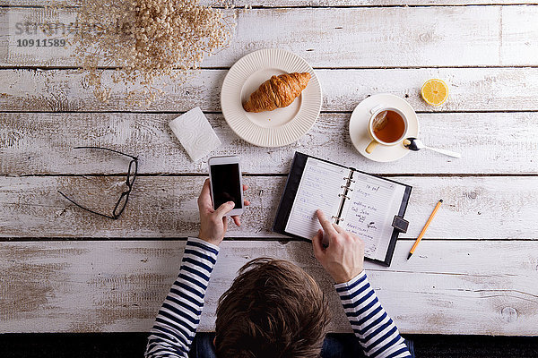 Mann arbeitet mit Smartphone und persönlichem Organizer während des Frühstücks