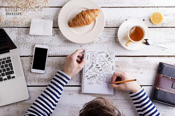 Mann bei Tisch mit Croissant und Tee  Notizen machend