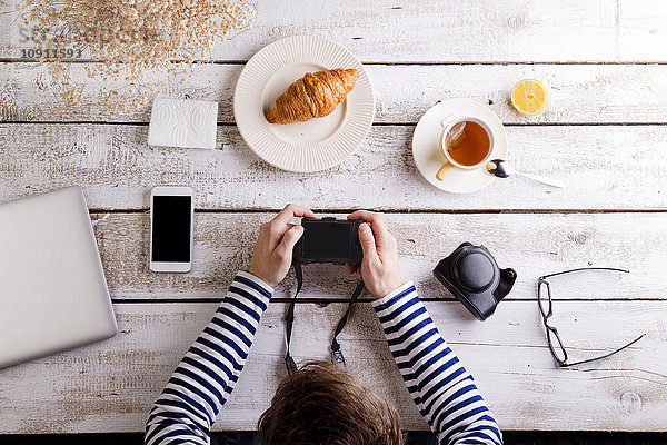 Mann  der am Tisch mit Croissant und Tee arbeitet  schaut auf seine Kamera.
