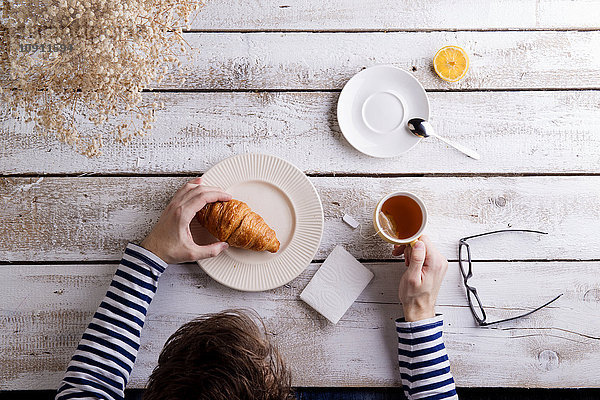 Mann am Tisch sitzend mit Tee und Croissant