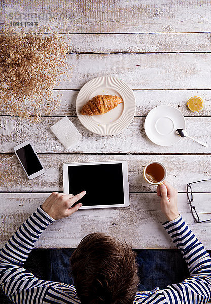 Mann  der am Tisch mit Croissant und Tee arbeitet  mit digitaler Tablette