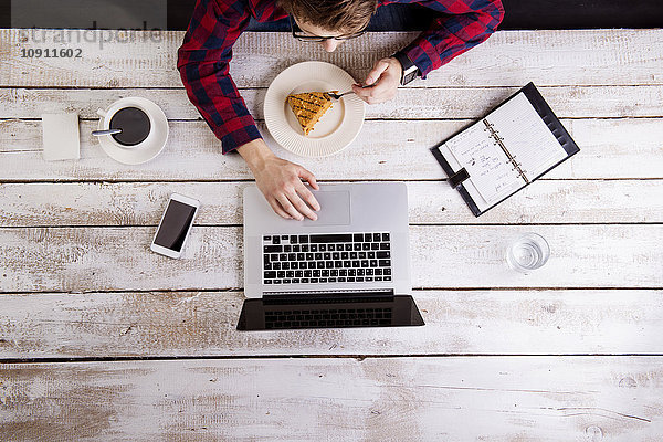 Mann arbeitet am Laptop bei Kaffee und Kuchen