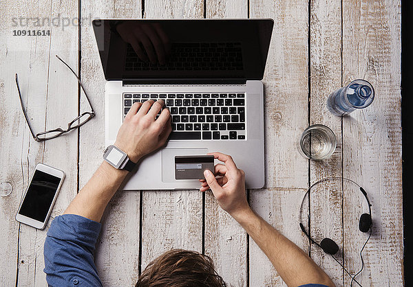 Mann sitzt am Schreibtisch und bezahlt online mit Kreditkarte.