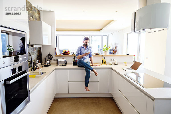 Mann sitzt in der Küche mit Smartphone