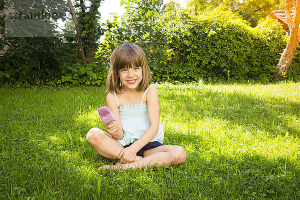 Porträt eines glücklichen kleinen Mädchens auf einer Wiese mit Heidelbeereis-Lolly