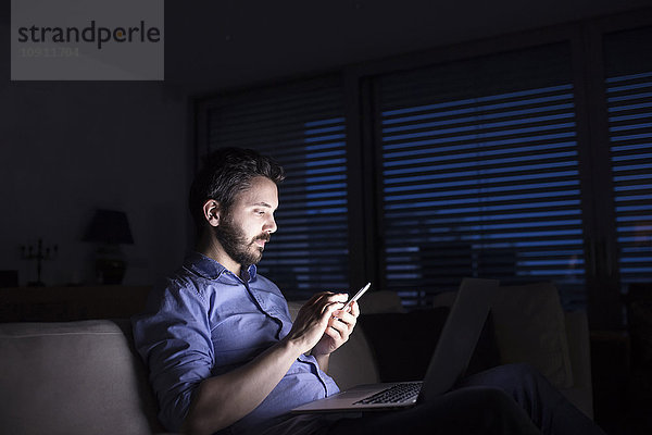 Mann arbeitet nachts mit Smartphone und Laptop