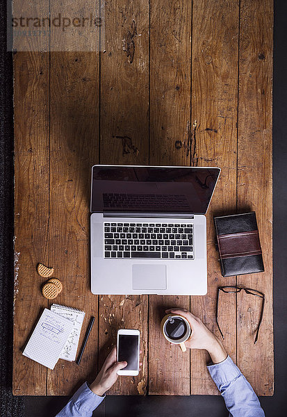 Mann mit Kaffeetasse und Smartphone am Schreibtisch