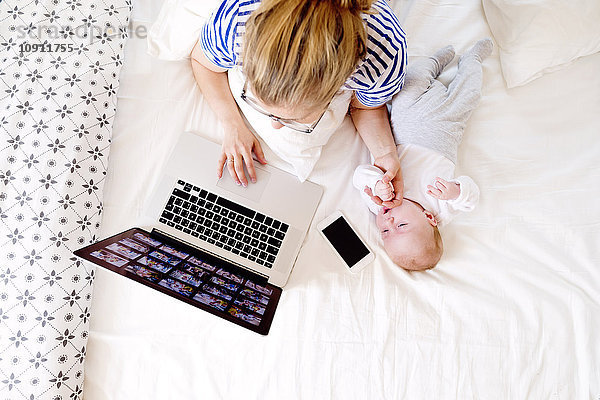 Mutter mit Baby zu Hause bei der Arbeit mit dem Laptop