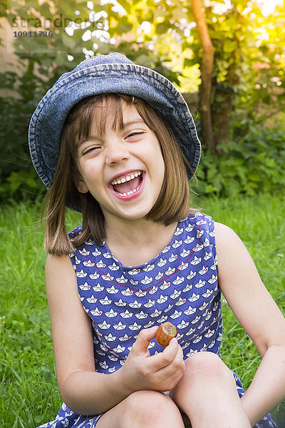 Porträt eines lachenden kleinen Mädchens auf einer Wiese mit Stachelbeere