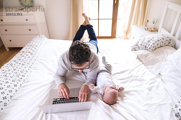 Vater mit Baby auf dem Bett liegend mit Laptop