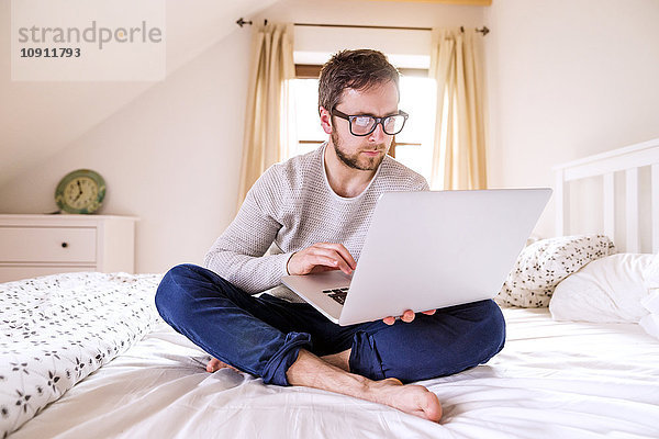 Mann auf dem Bett sitzend mit Laptop