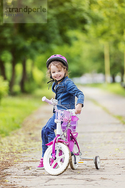 Lächelndes Mädchen auf dem Fahrrad mit Stützrädern