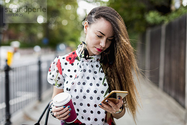 Porträt einer jungen Frau mit Kaffee zum Anschauen ihres Smartphones