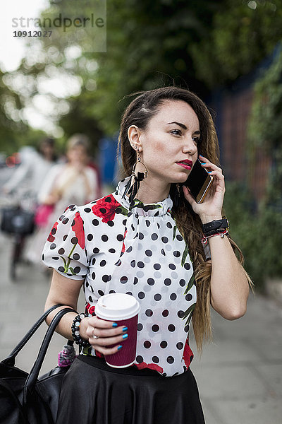 Portrait einer jungen Frau mit Kaffee zum Telefonieren mit Smartphone