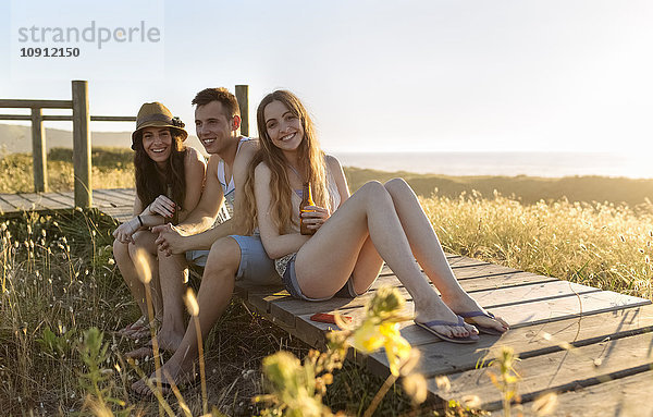 Freunde sitzen an der Strandpromenade und trinken bei Sonnenuntergang Bier.