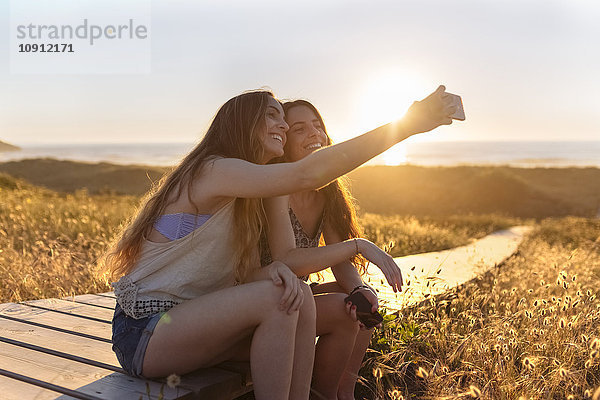 Junge Frauen  die sich bei Sonnenuntergang an den Strand setzen