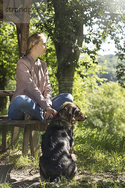 Junge Frau sitzt auf einer Holzbank und entspannt sich mit ihrem Hund.