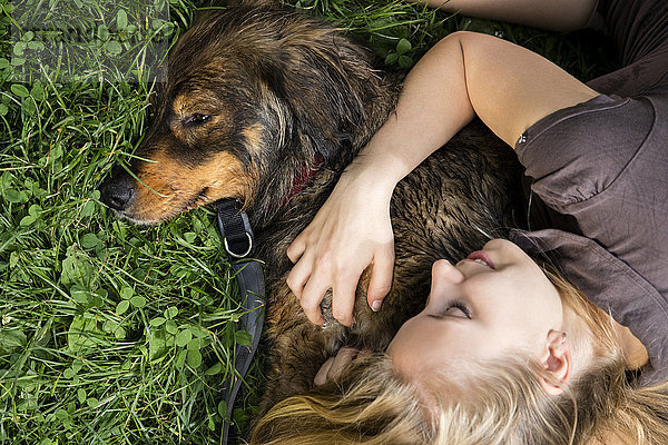 Junge Frau entspannt sich mit ihrem Hund auf einer Wiese
