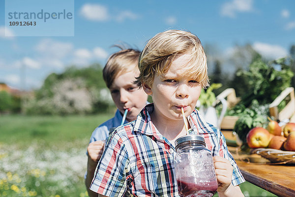 Zwei Jungen im Freien  die aus Gläsern trinken.