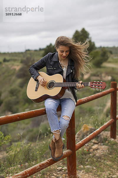 Frau auf Holzzaun sitzend Gitarre spielend