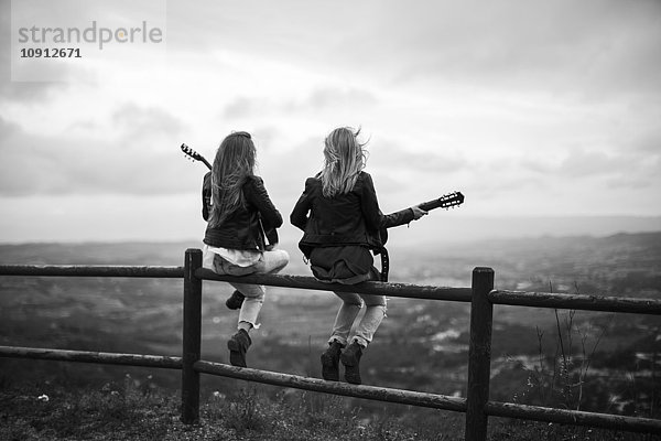 Zwei Frauen sitzen auf Holzzaun mit Gitarren