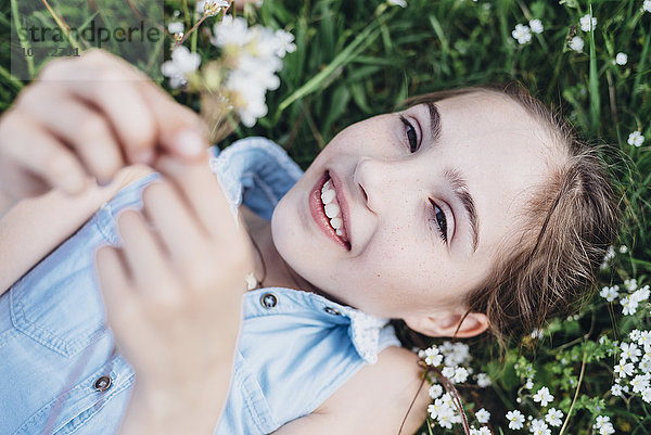 Lächelndes Mädchen auf Blumenwiese liegend